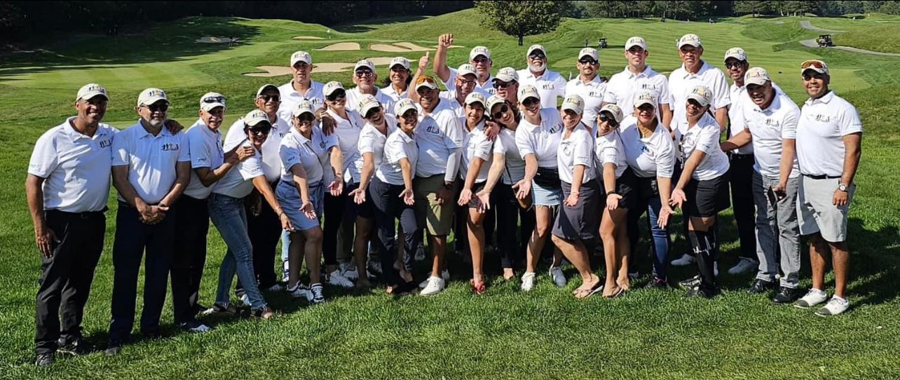 Group of people, mostly men, on a golf course wearing white shirts and hats.
