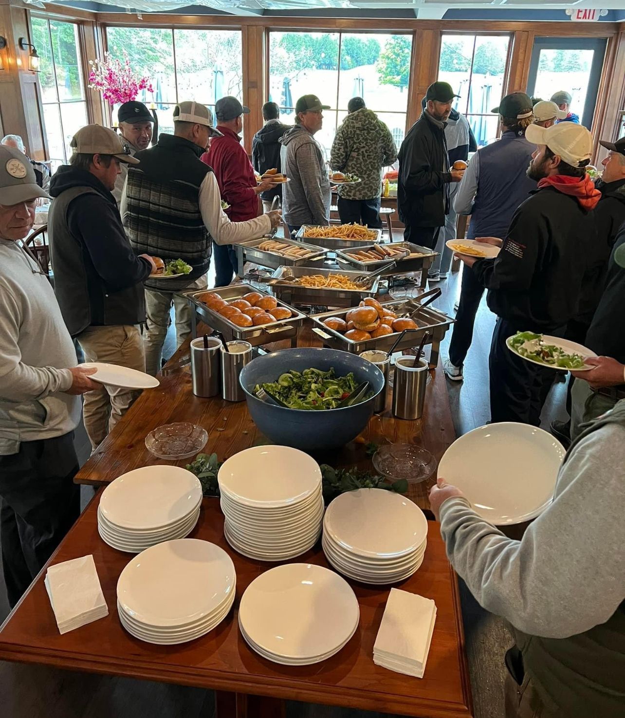 People at a buffet table; a variety of food in serving dishes; wood table, white plates and napkins.