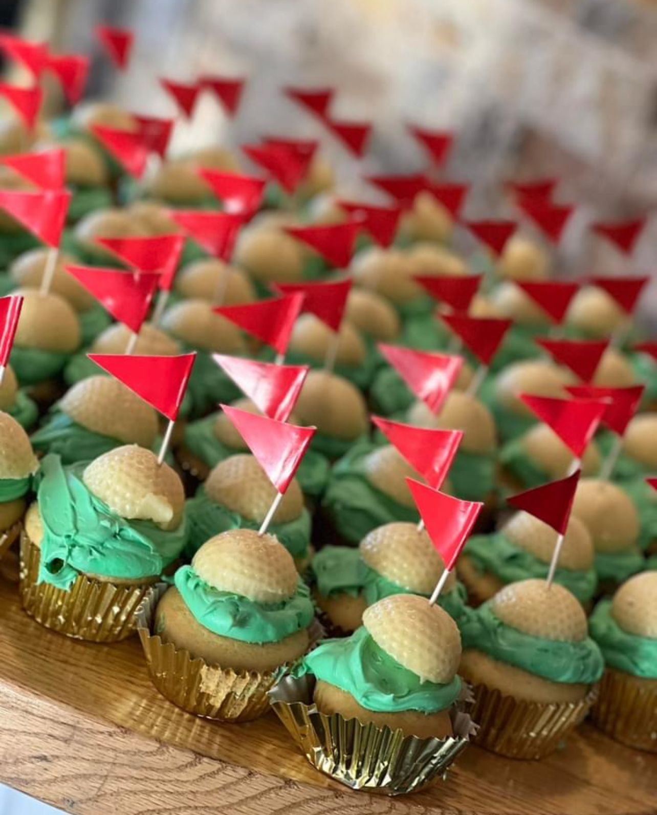 Cupcakes decorated like golf balls with green frosting and red flag toppers, on a gold tray.