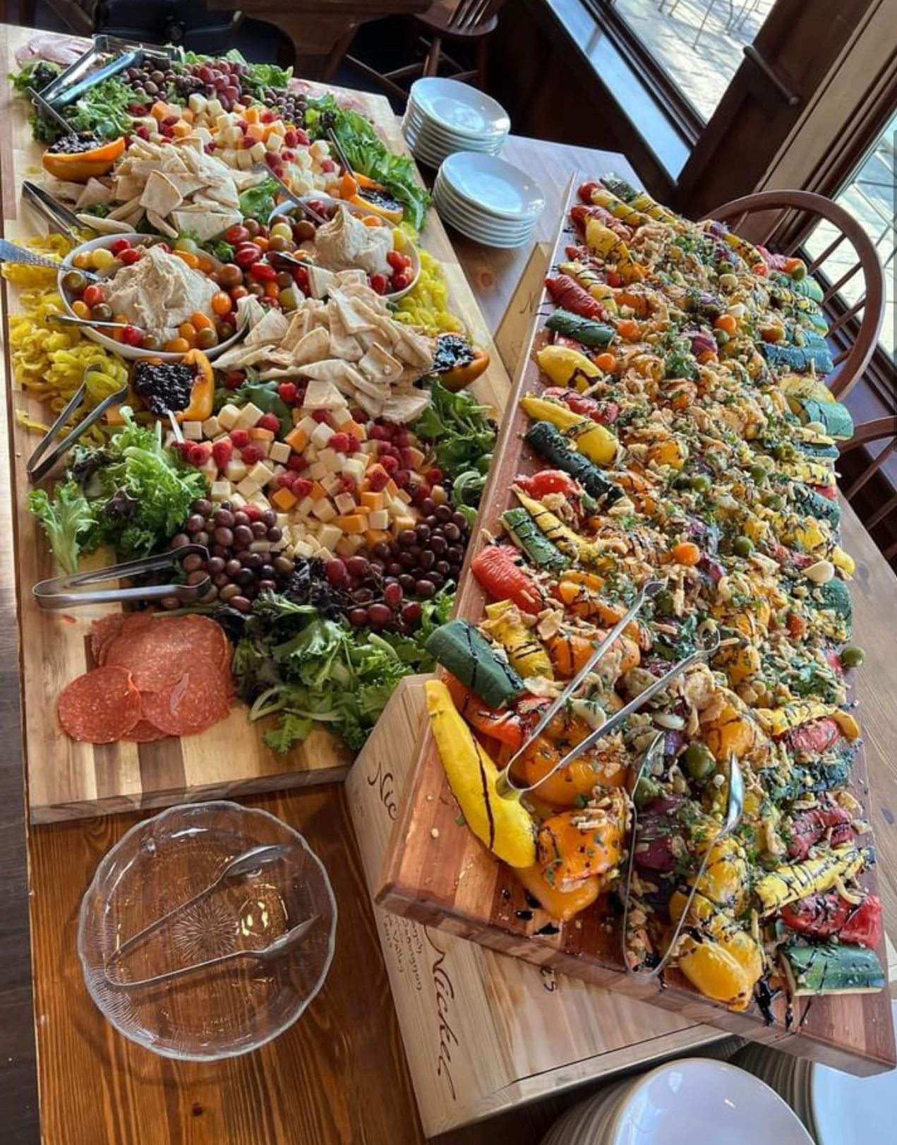 Two large wooden serving boards laden with colorful food for a gathering, on a wooden table.