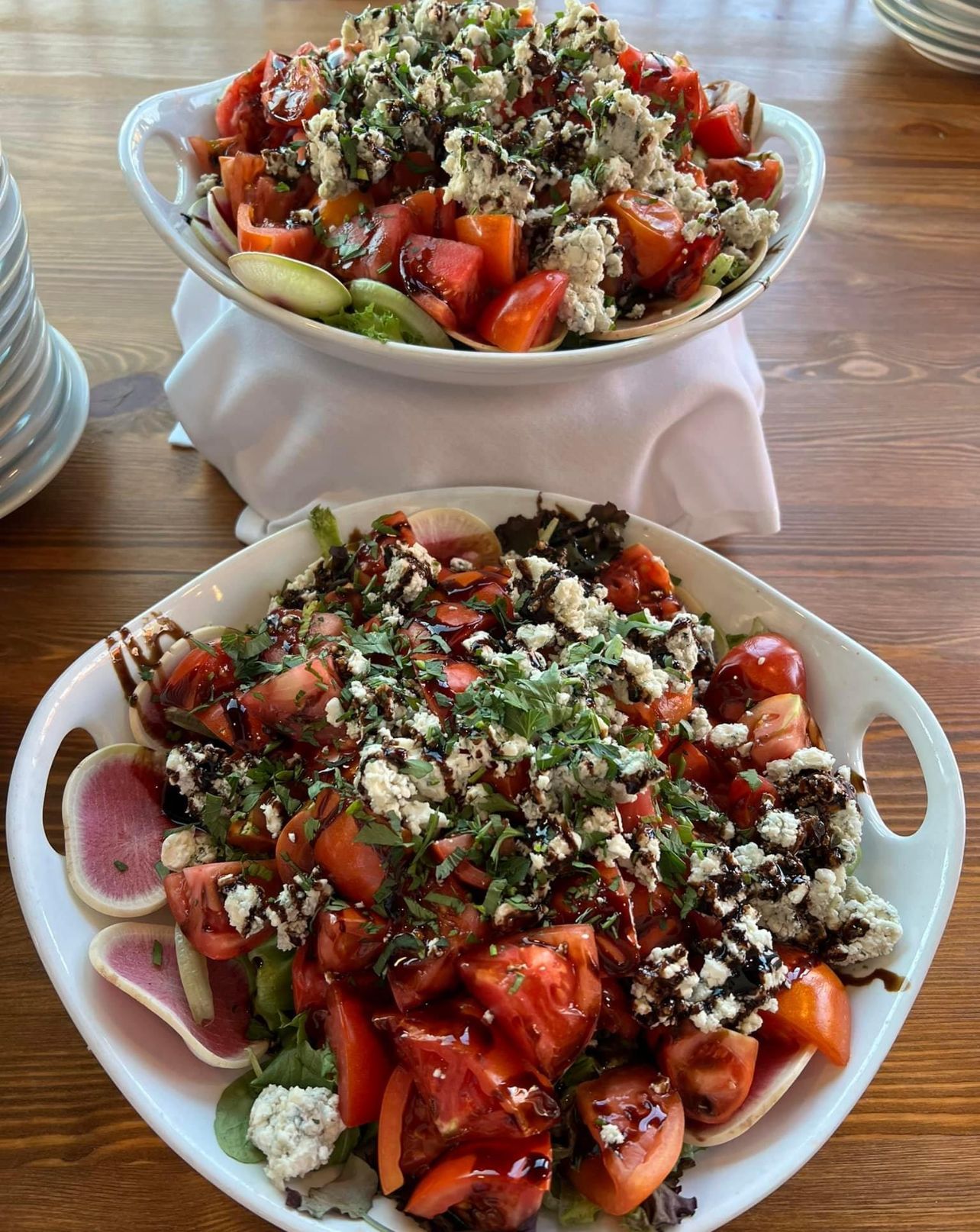 Two tomato and cheese salads in white oval dishes on a wooden table.