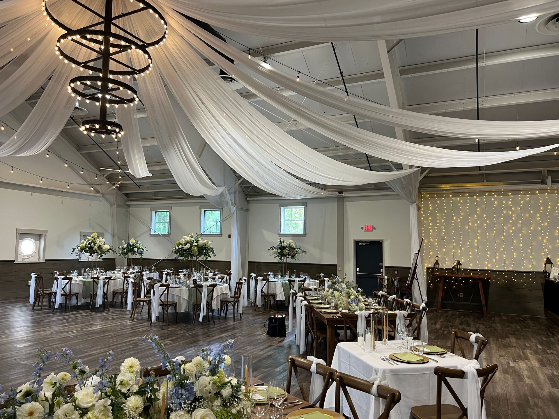 Wedding reception with white draped ceiling, tables set with flowers, and wooden floors.
