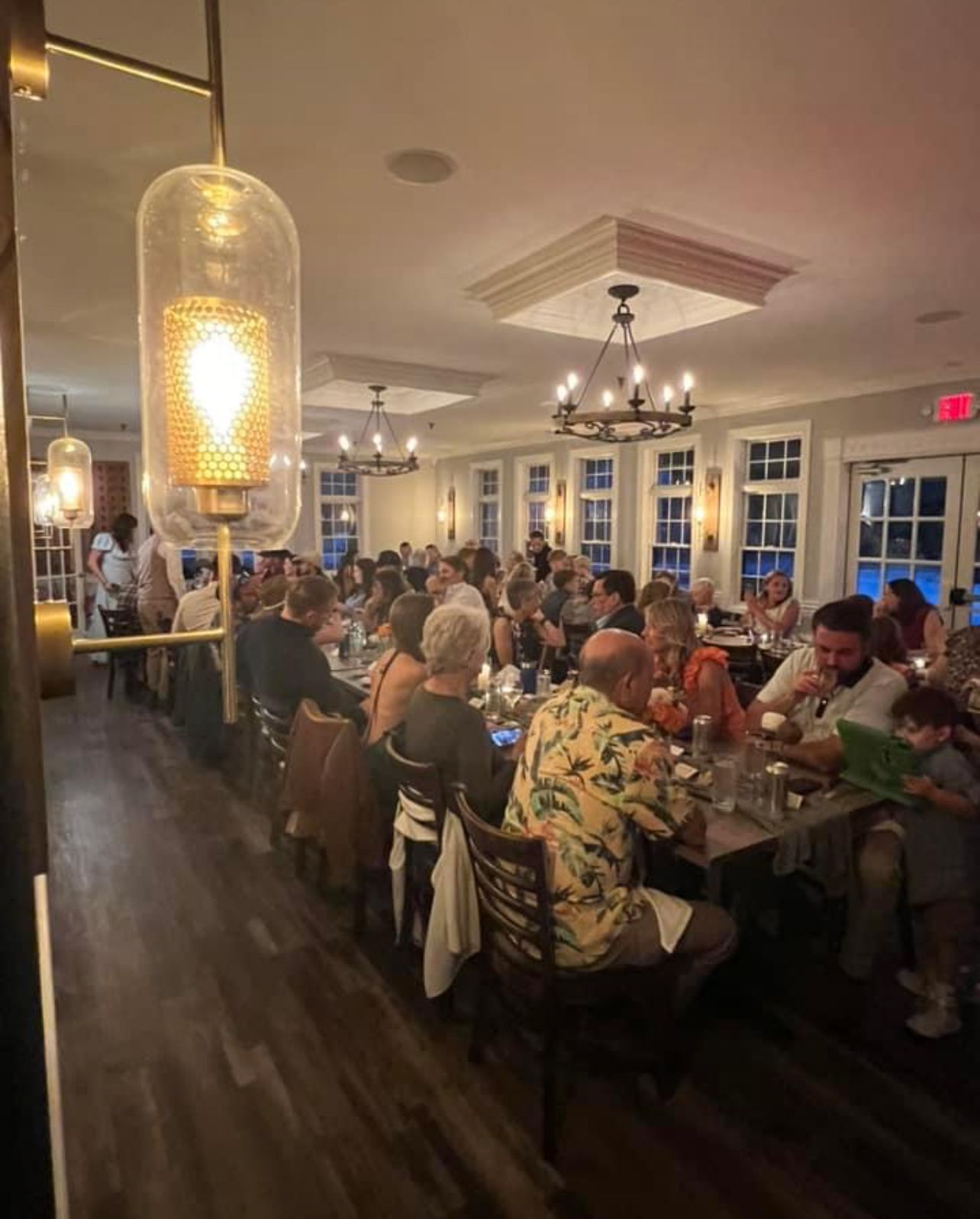Restaurant interior with a long table of people dining; warm lighting.