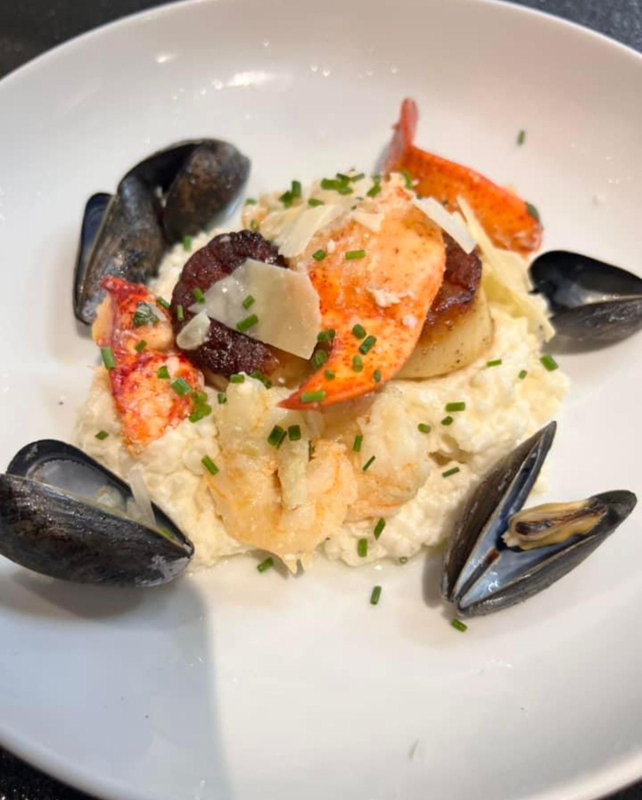 Seafood risotto with lobster, scallops, mussels, shrimp, and shaved parmesan cheese, garnished with chives.