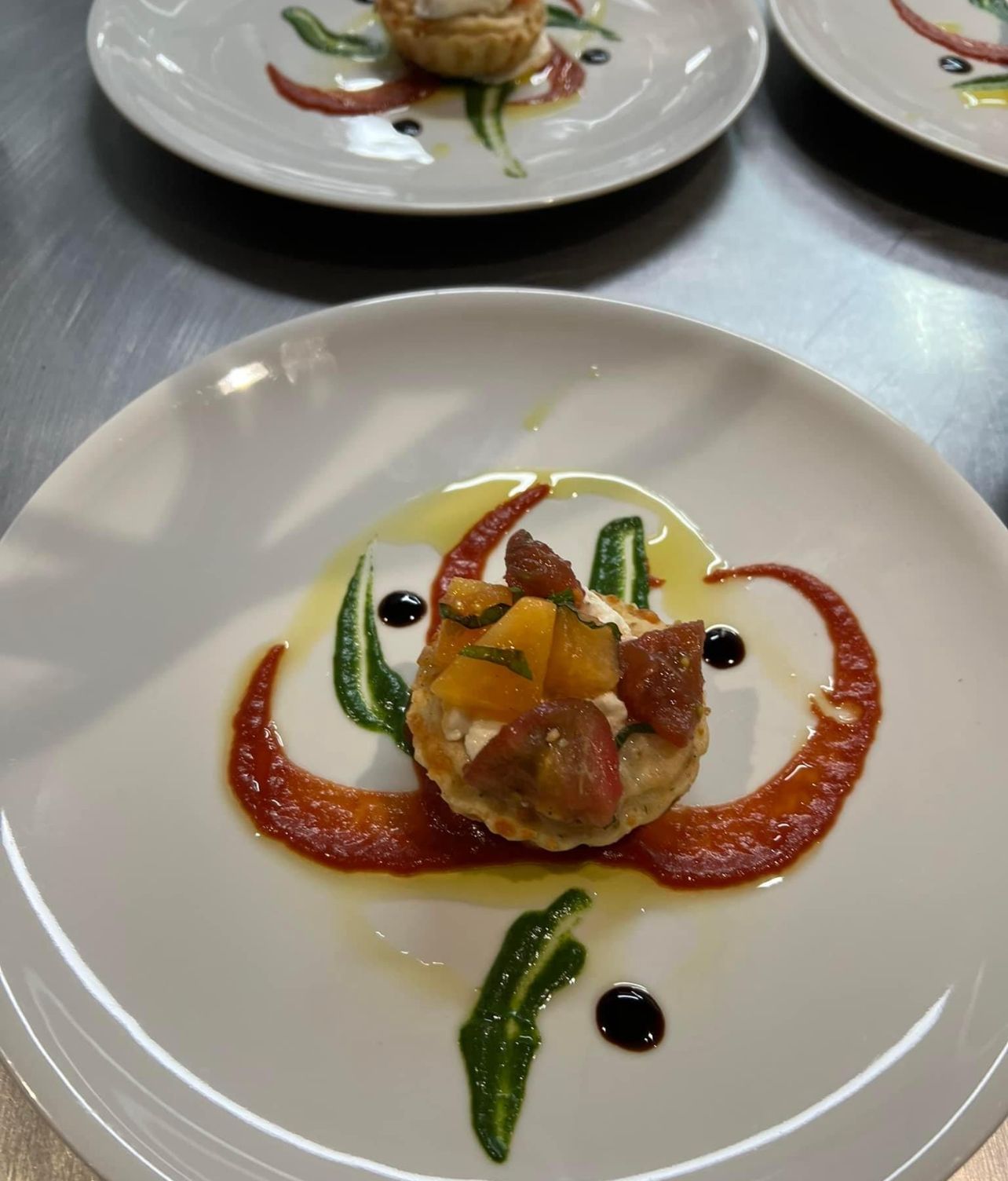 Individual plated tart with red sauce, green sauce, and orange topping on white plates.