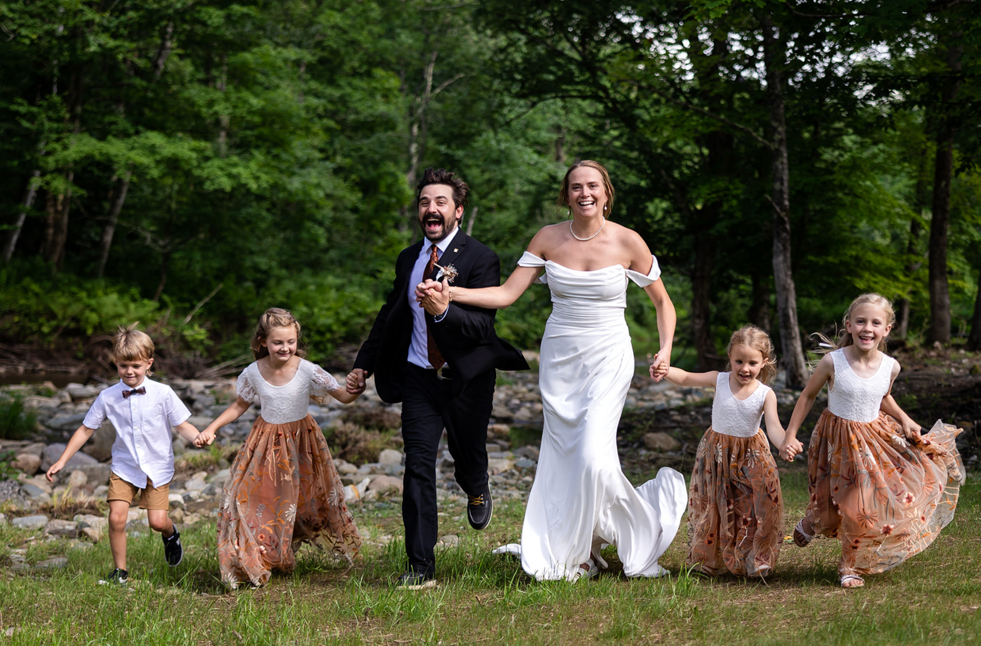 Bride, groom, and children running joyfully in a field on their wedding day.
