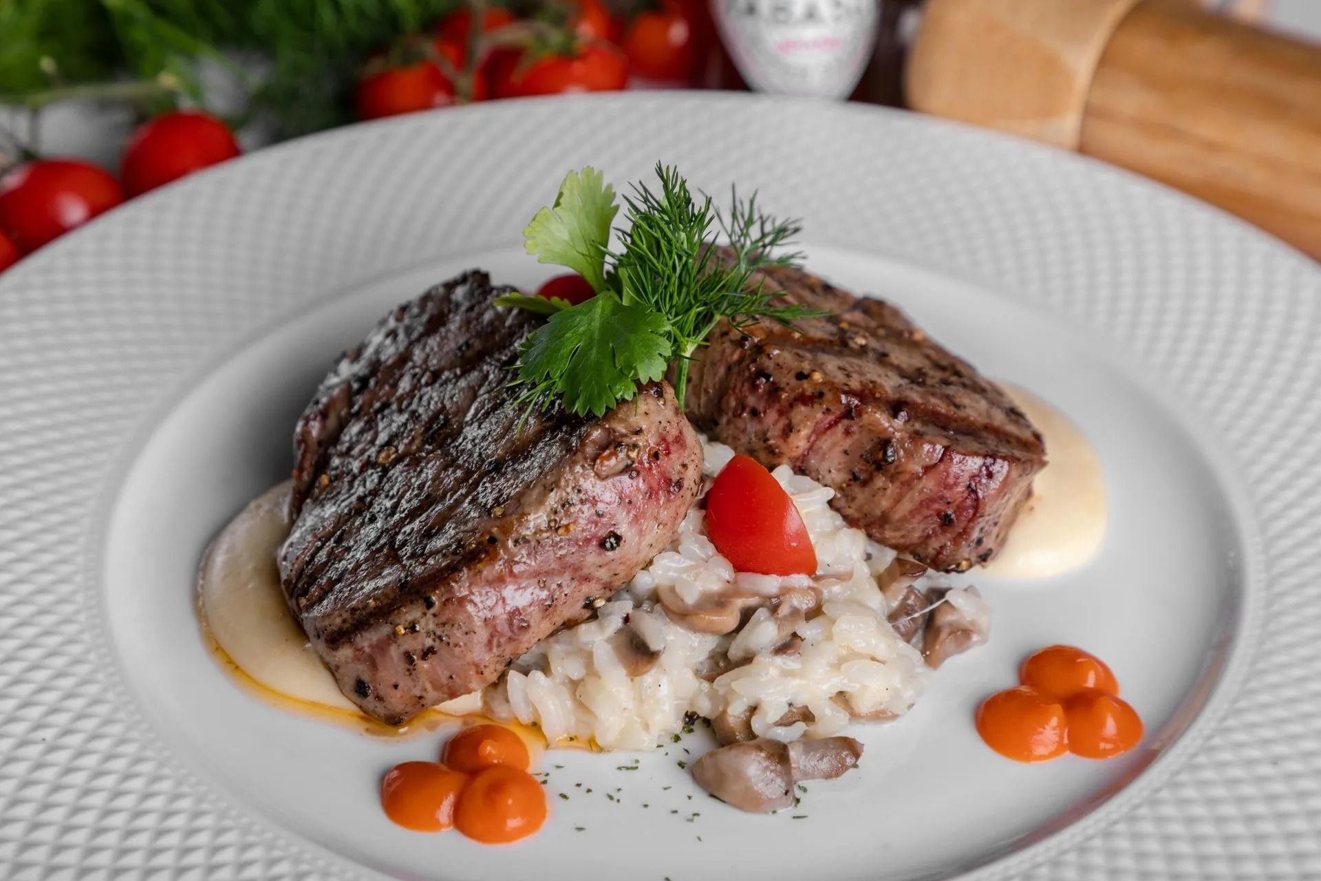 Grilled steak with risotto, cherry tomatoes, and sauce on a white plate.