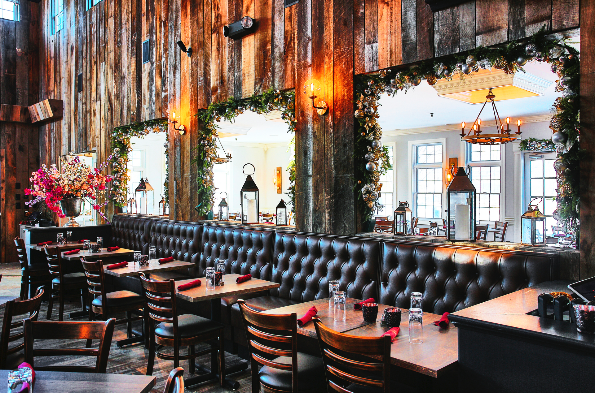 Cozy restaurant interior with wooden walls, leather booths, tables set for dining, and mirrors.