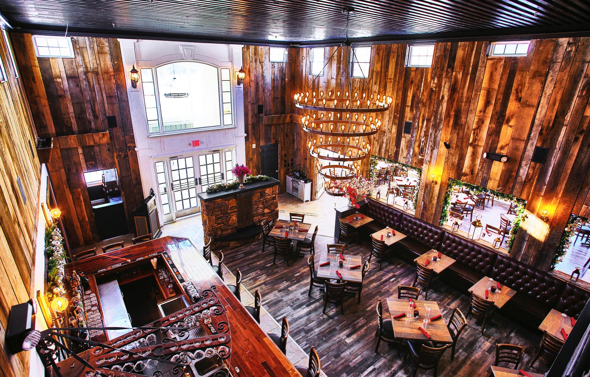 High-angle view of a rustic restaurant interior with wood paneling, a bar, tables, and a chandelier.
