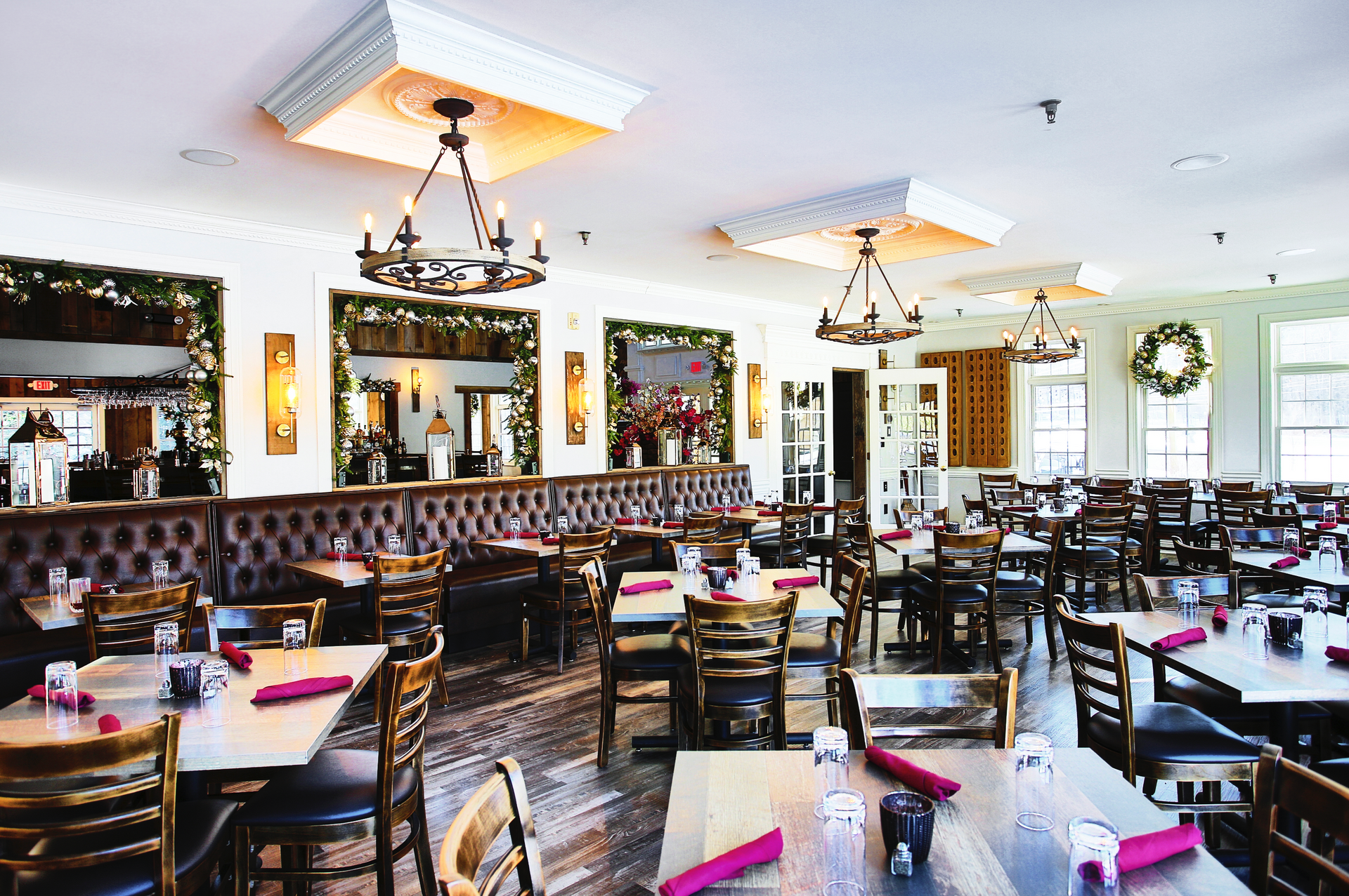 Restaurant interior with tables, chairs, chandeliers, and booths. White walls, dark furniture, and wood floors.