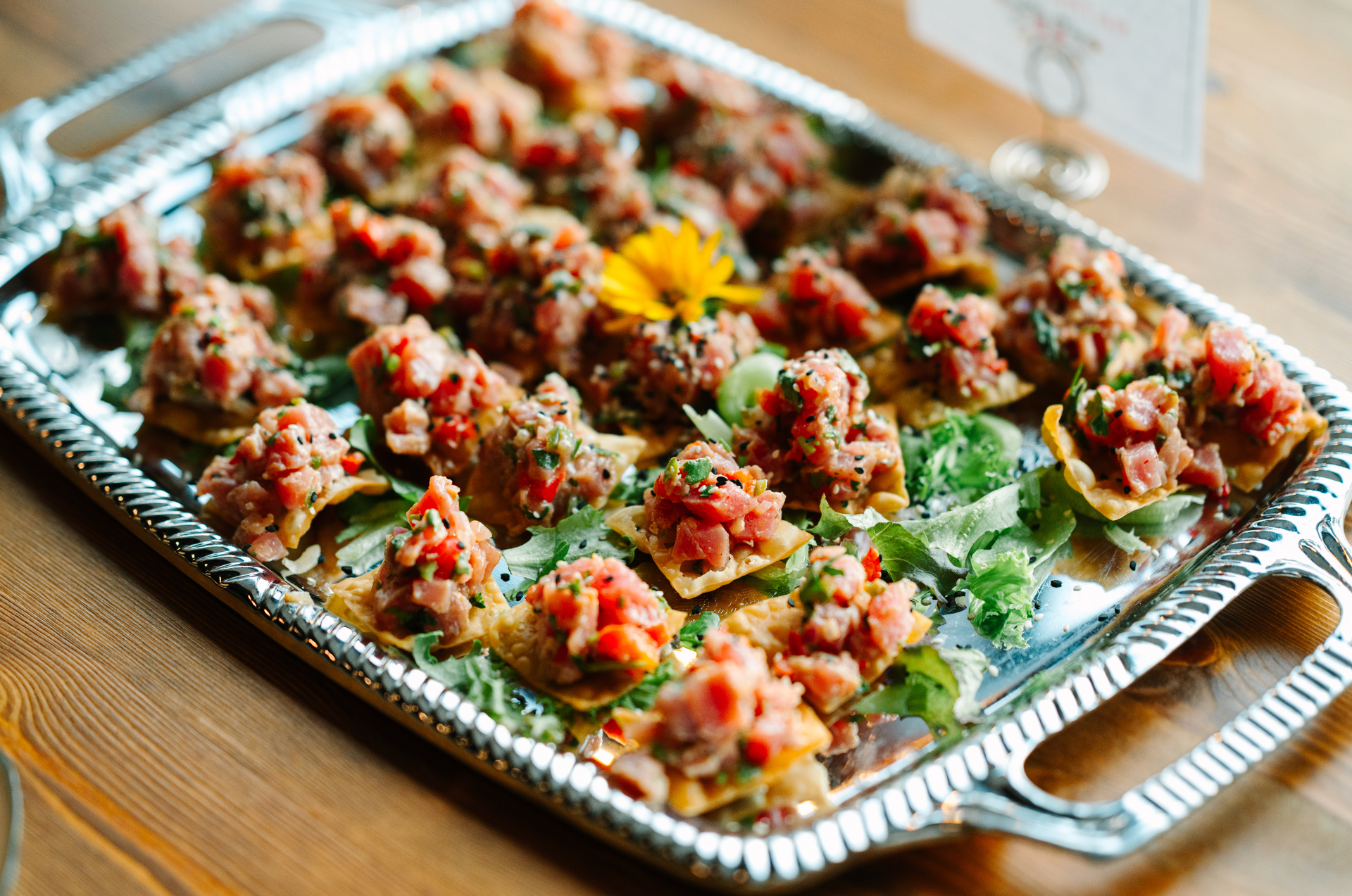 Appetizer tray with small bites of tuna tartare on crackers, garnished with greens.