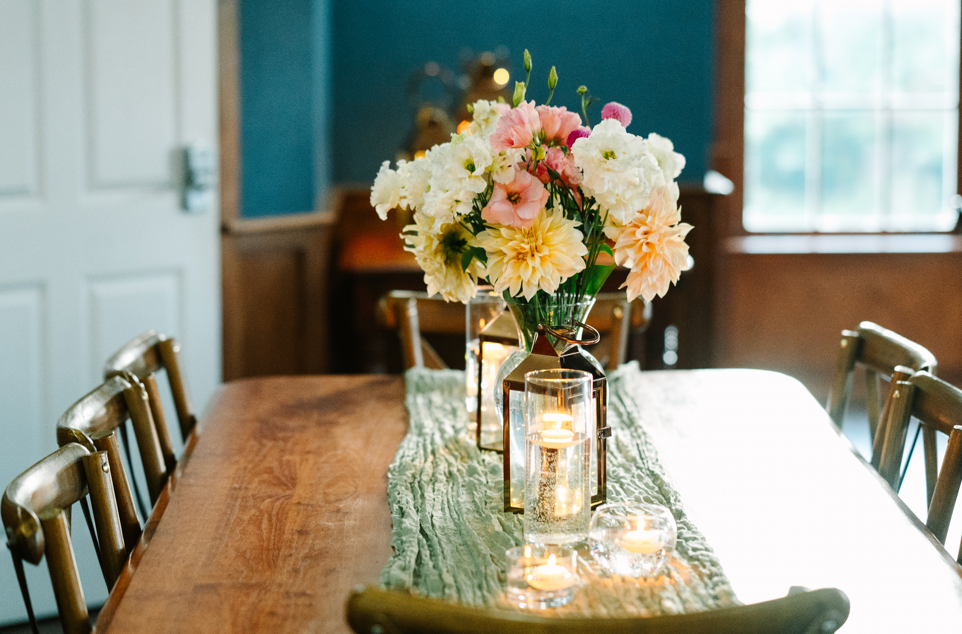 A wooden dining table with a floral centerpiece and lit candles.