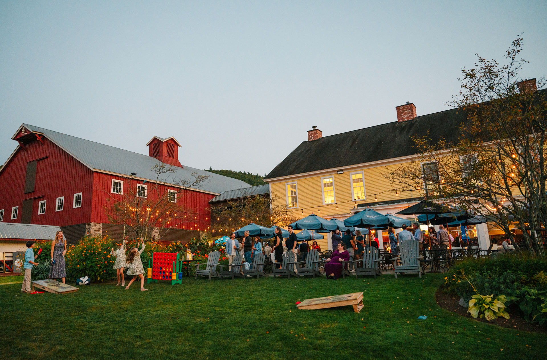 Outdoor gathering with red barn, people socializing on grass, playing games.