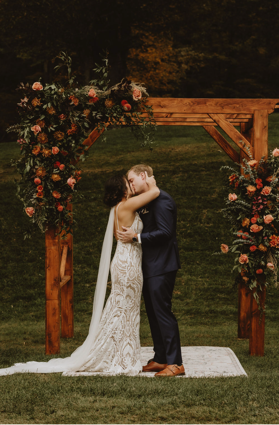 A bride and groom are kissing under a wooden arch at their wedding ceremony.