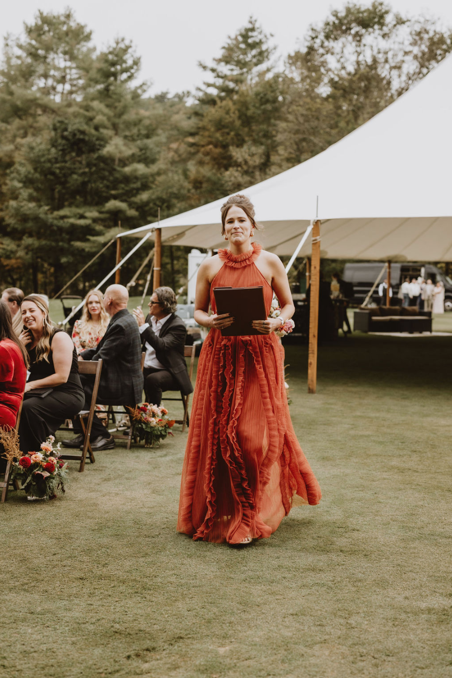 A woman in a red dress is walking down the aisle at a wedding.