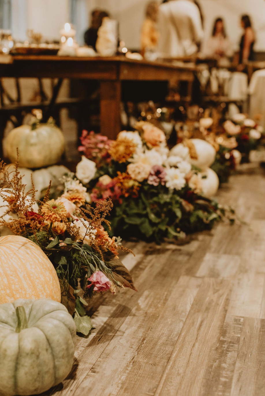 A row of pumpkins and flowers on the floor in a room.