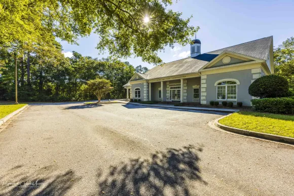 bank of the lowcountry's ravenel blue and white building with a driveway leading to it is surrounded by trees .