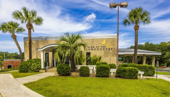 front of the bank of the lowcountry building in forest hills with palm trees in front of it .
