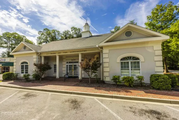 bank of the lowcountry's ridgeland branch building, a large tan and cream facility, with a lot of windows and landscaping with trees and shrubs in front of it .