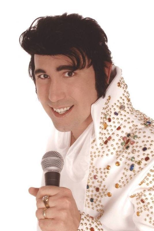 Smiling performer in a white rhinestone jacket holding a microphone