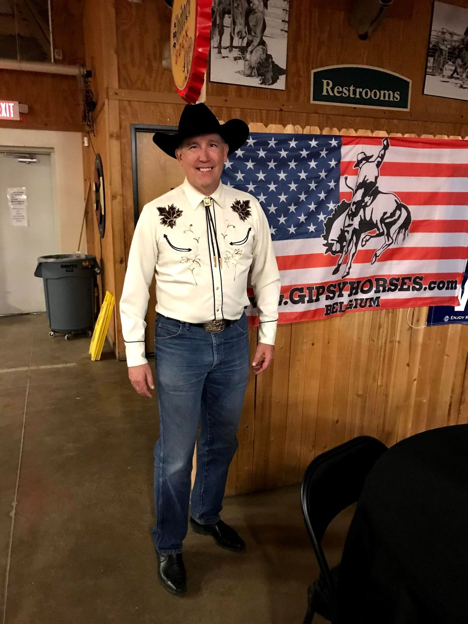Person in cowboy hat standing indoors beside a patriotic flag banner and “Restrooms” sign.
