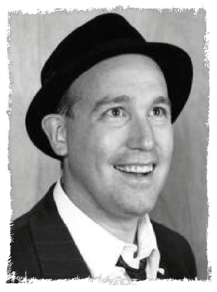 Black-and-white portrait of a smiling person in a dark hat and suit, looking upward