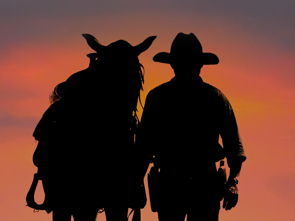 Two cowboy silhouettes against a red-orange sunset sky
