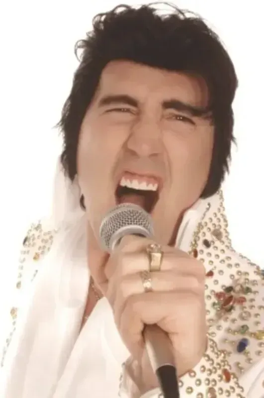 Singer belting into a microphone, eyes shut, wearing a white patterned outfit against a bright background