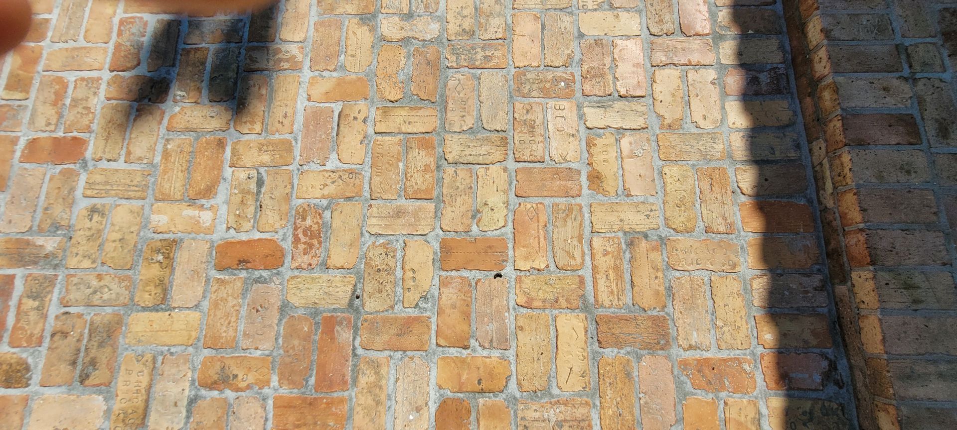 Brick-paved walkway with shadows from people and nearby structures