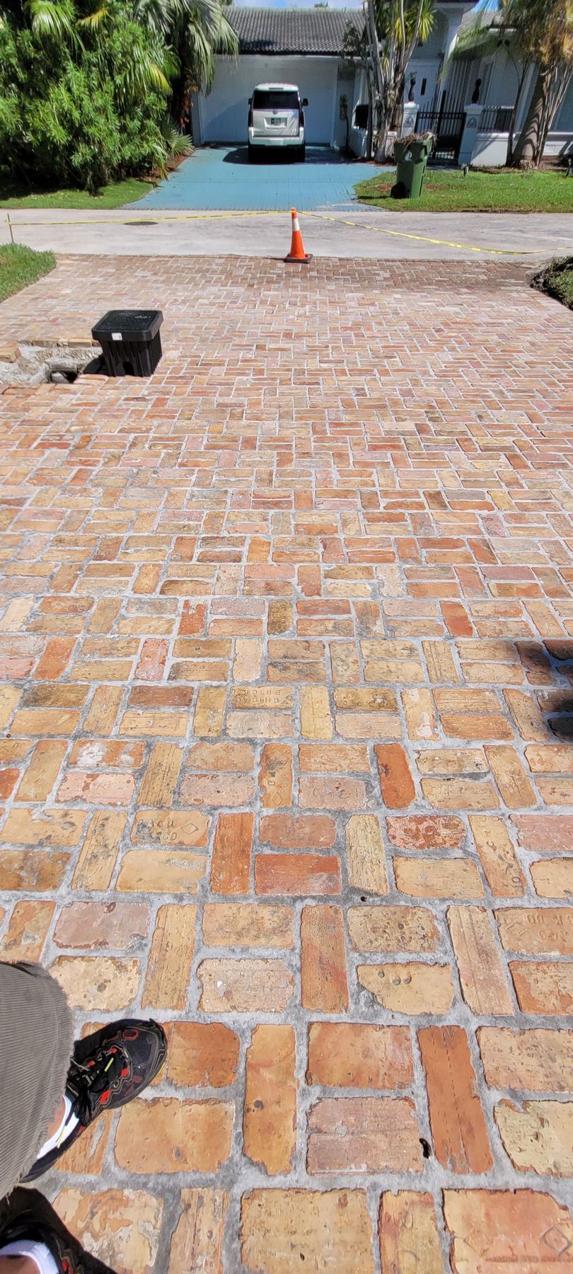 Brick driveway leading to a garage, with a parked white van and an orange cone ahead.