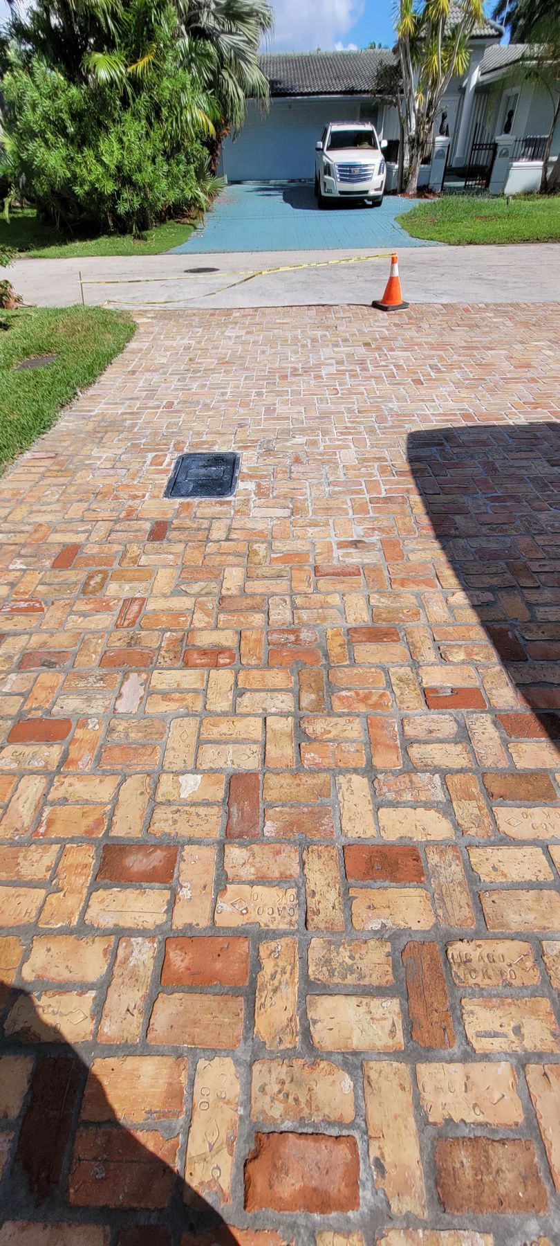 Brick driveway with a small black mat, orange cone near the street, and a white SUV in the background