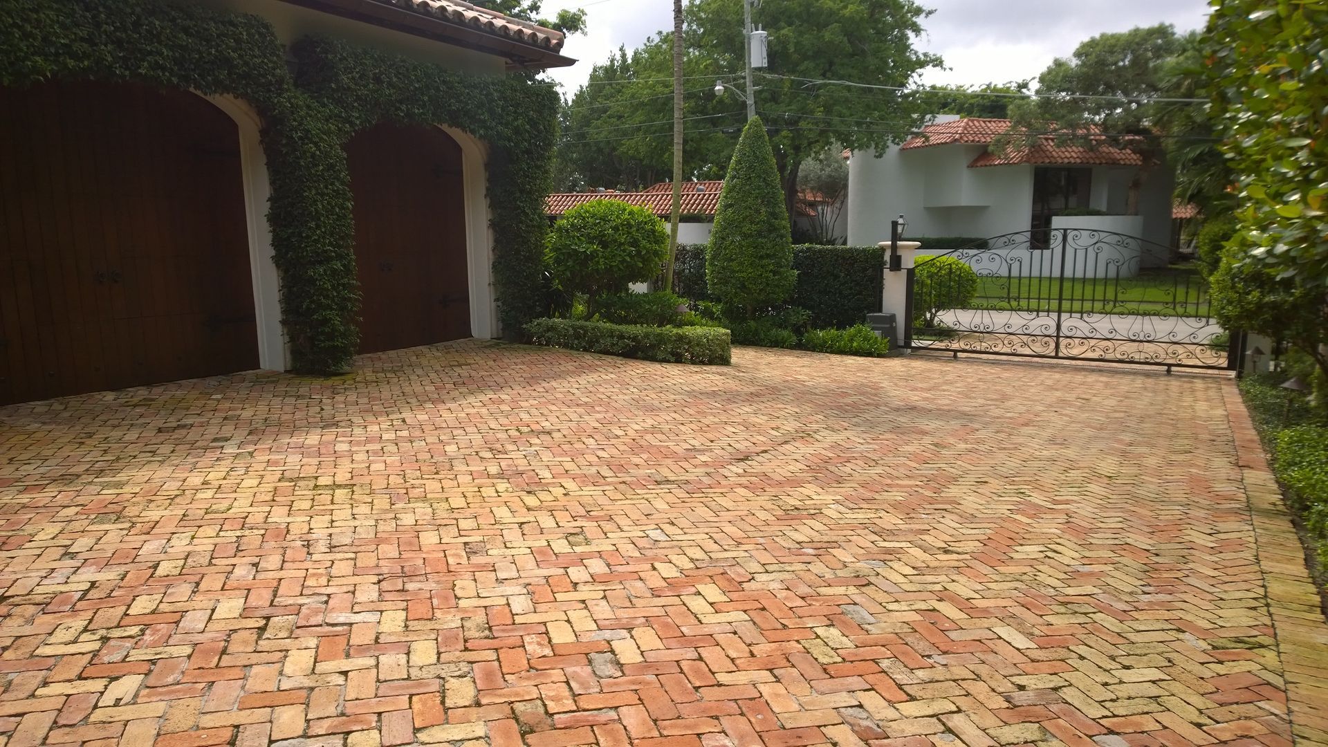 Brick-paved driveway beside a vine-covered garage, with trees and a white house in the background