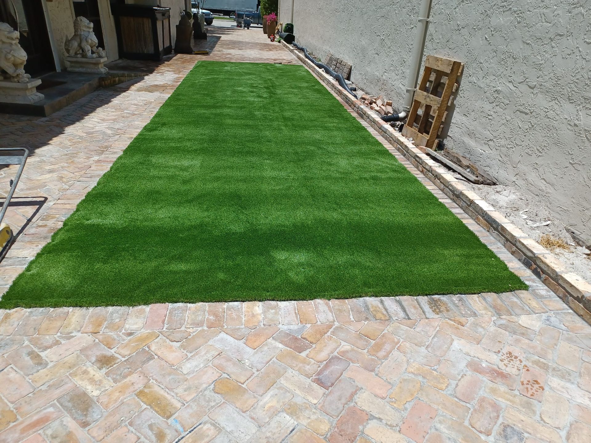Rectangular green artificial turf strip beside a stone walkway in a narrow outdoor courtyard