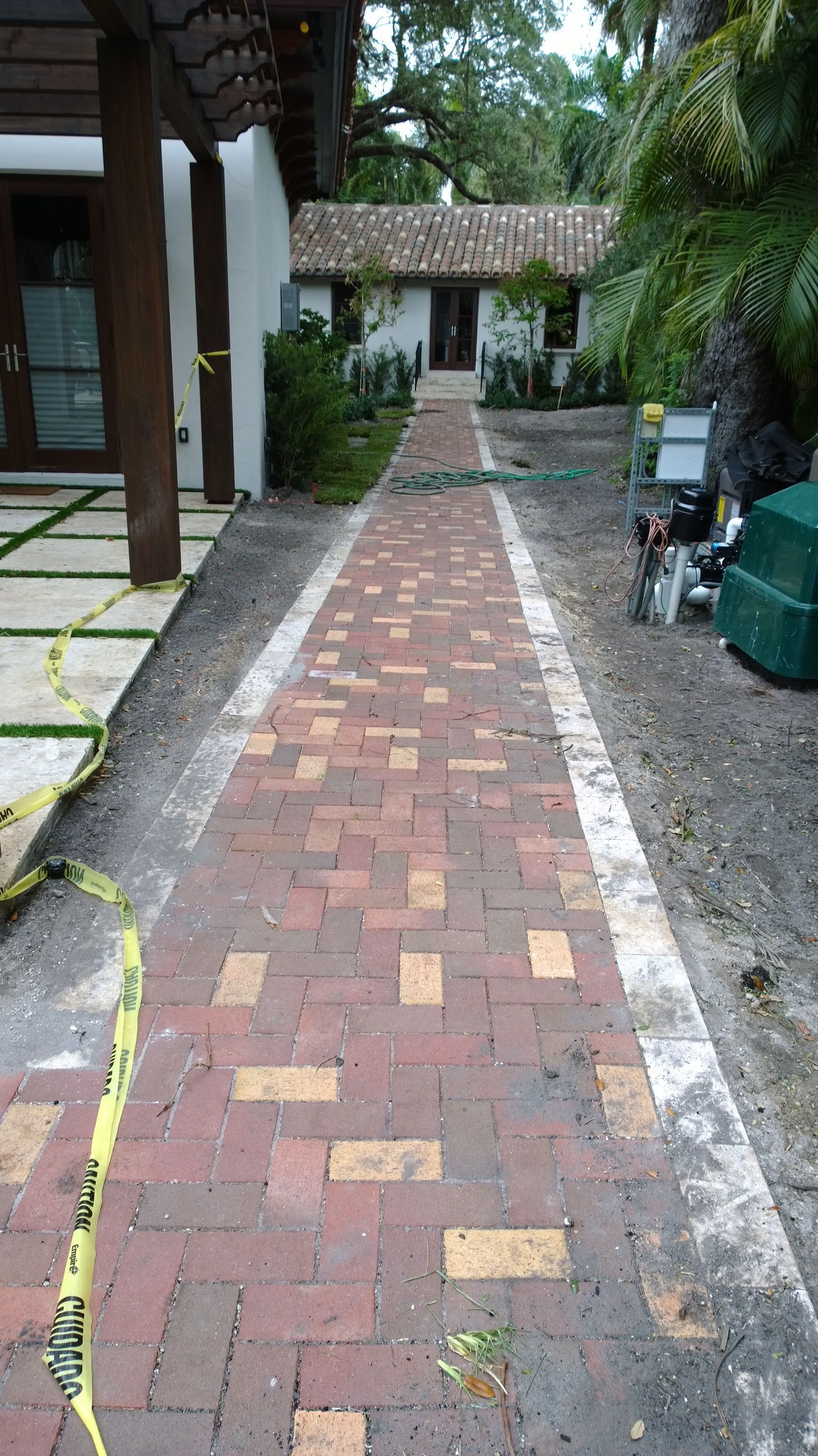 Narrow brick walkway leading to a small gate in a garden courtyard, bordered by greenery and stone paths