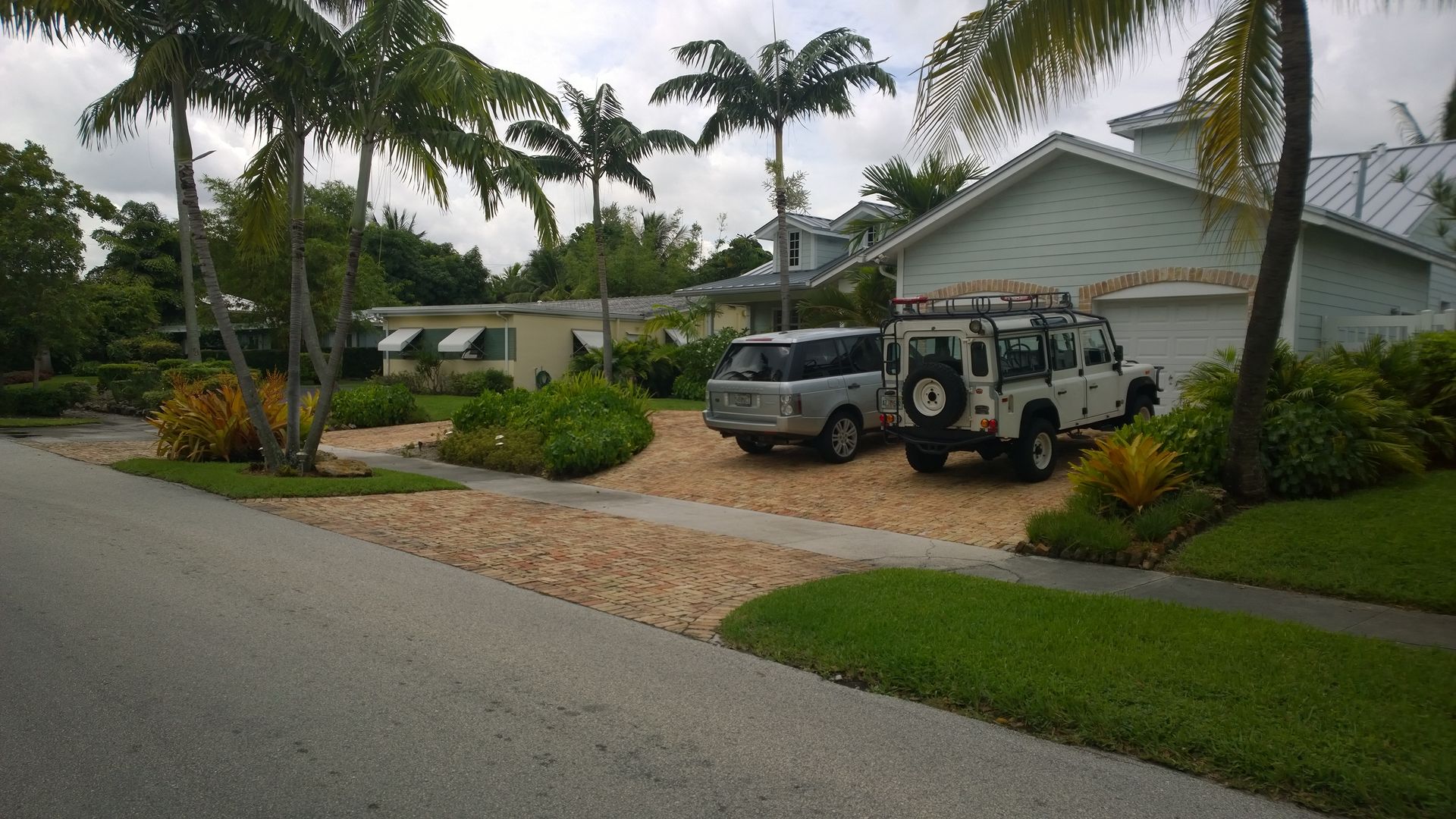 Suburban house with palm trees, two parked vehicles, and a wet driveway after rain