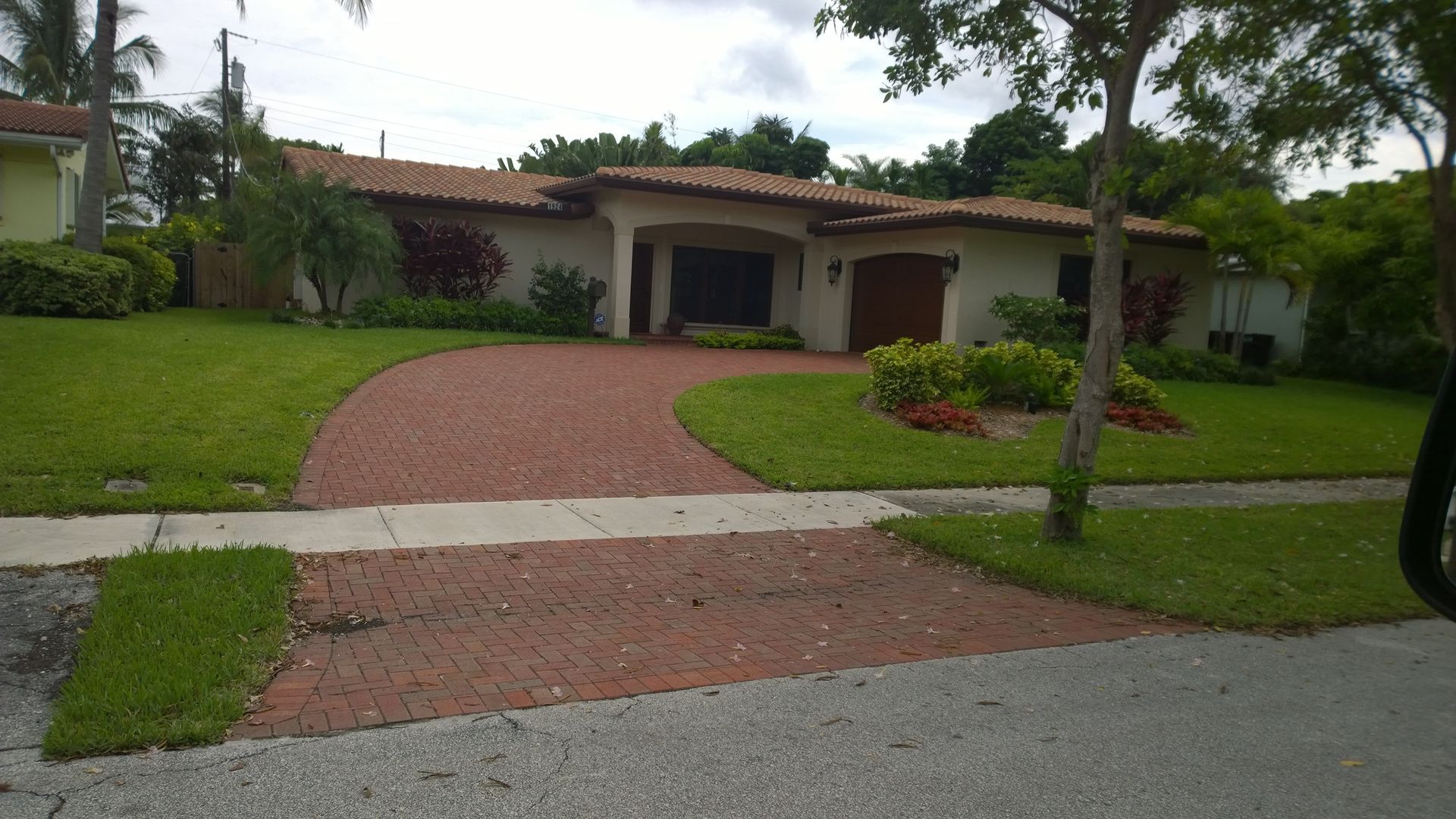 Single-story house with red tile roof, green lawn, and a curved brick driveway under trees