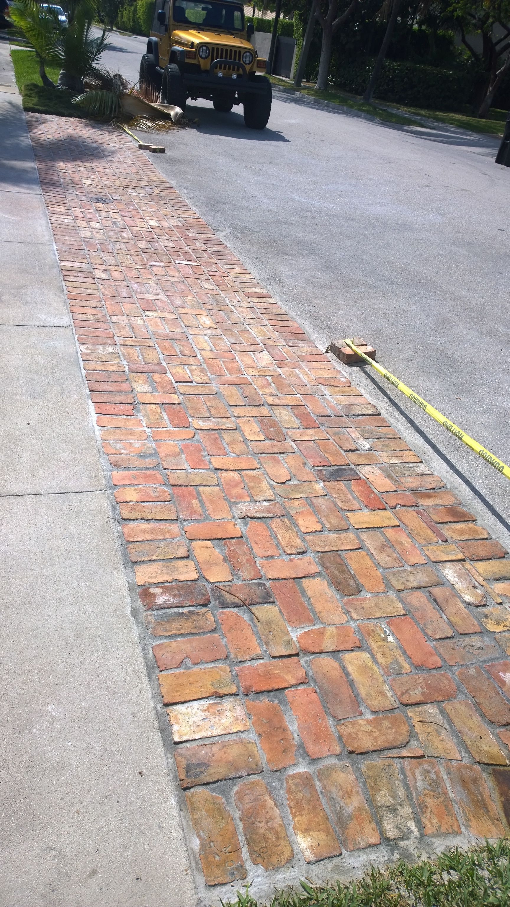 Brick sidewalk repair beside a road, with loose bricks and a utility vehicle in the background