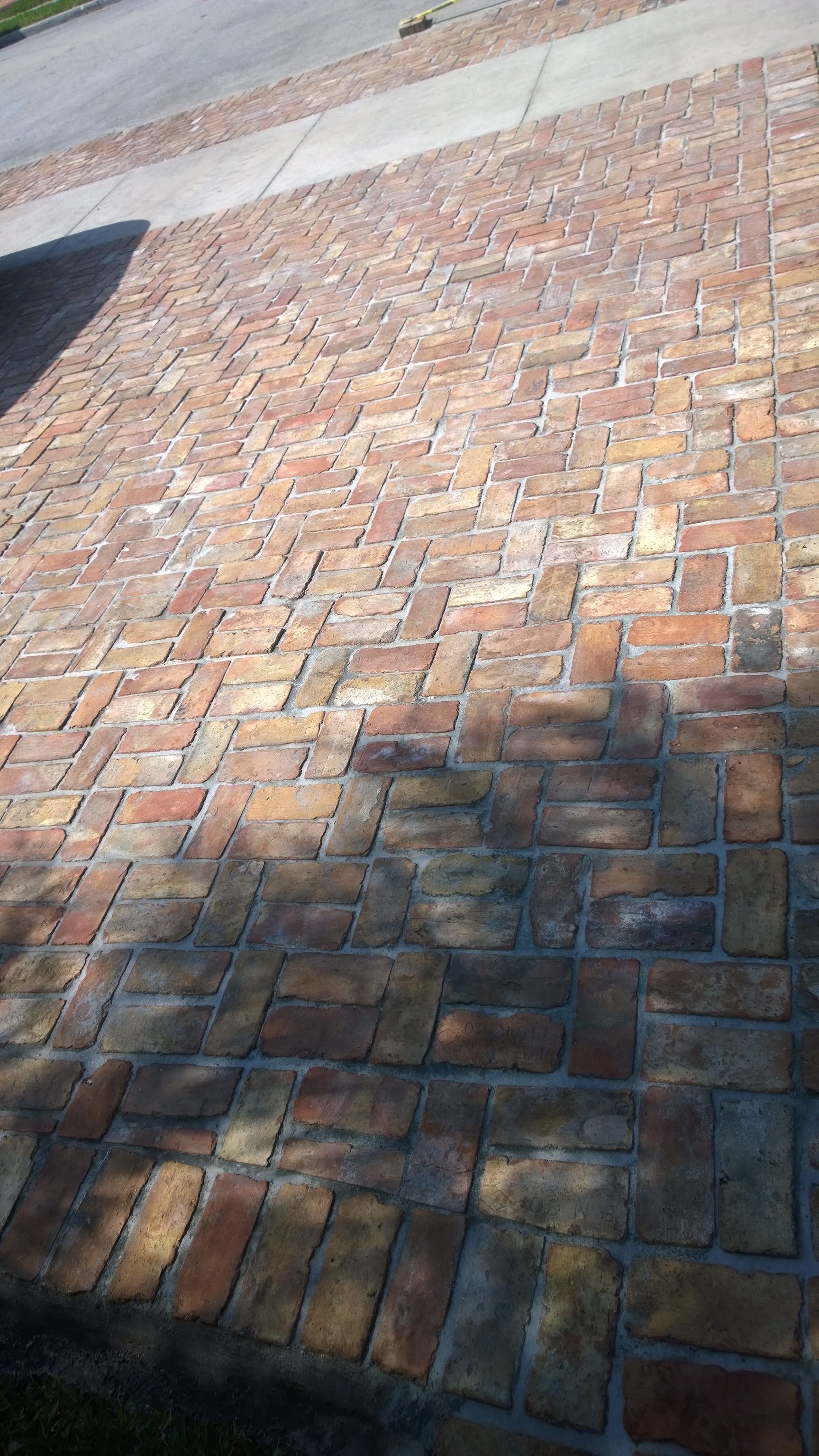 Brick-paved driveway or walkway in sunlight and shadow with a curb at the top