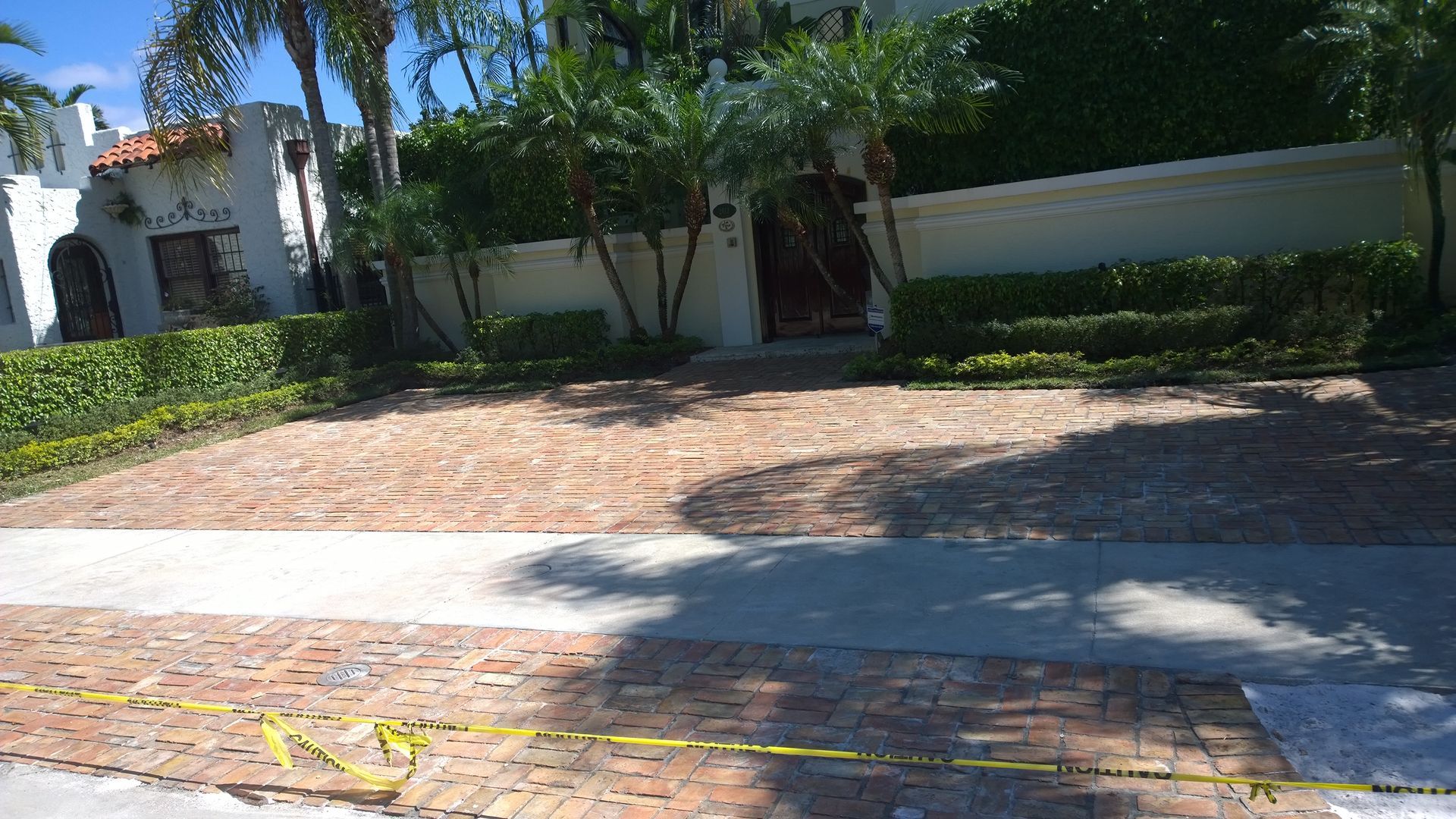 Sunny driveway in front of a white stucco house with palm trees and brick paving