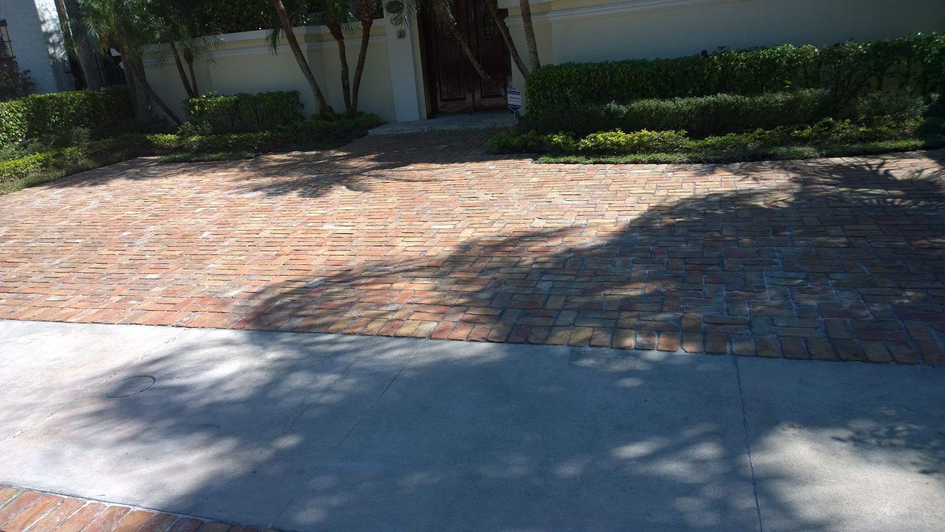 Brick-paved courtyard beside a sidewalk, with trees and building shadows in sunlight