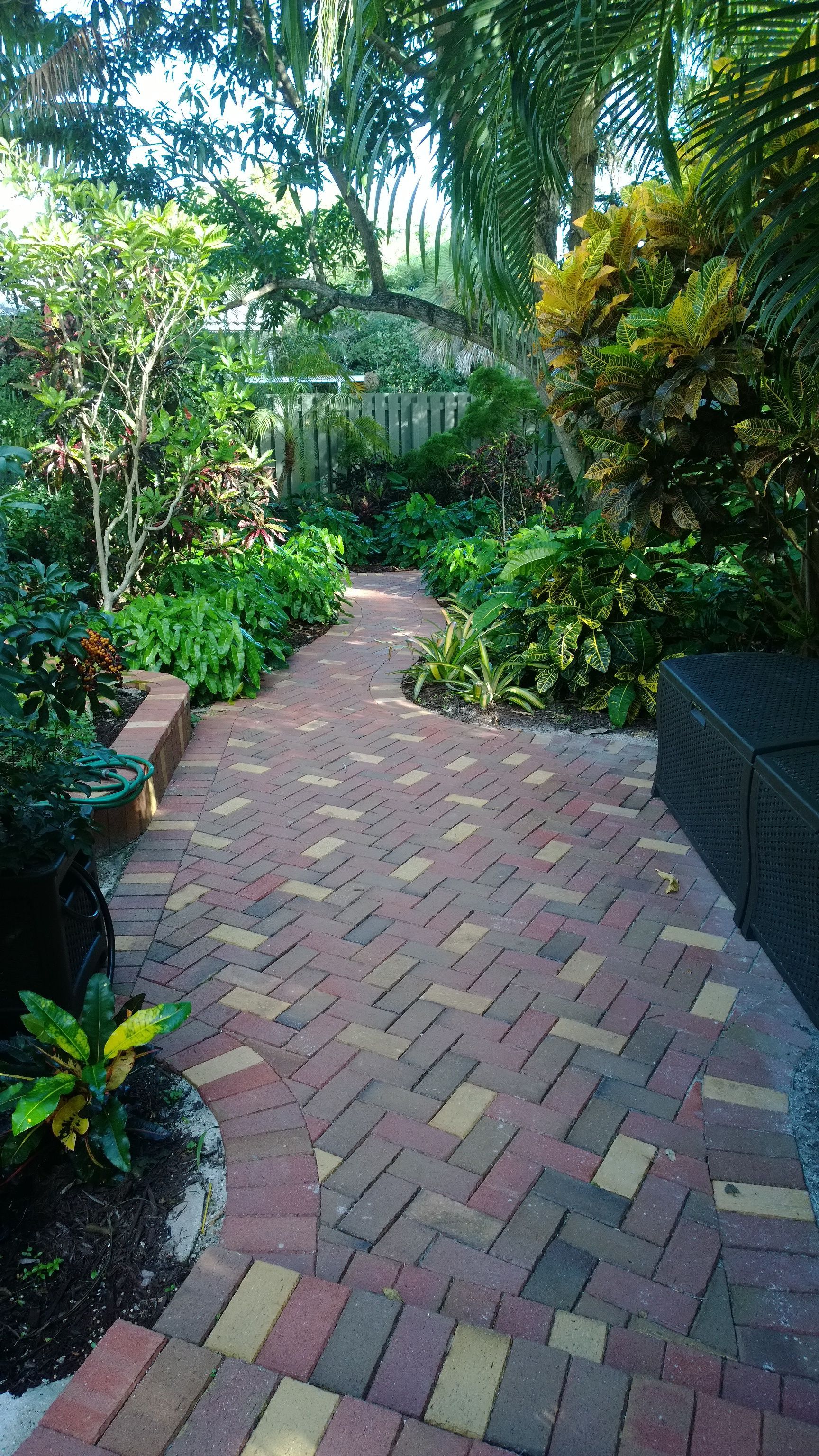 Brick garden path winding through lush tropical greenery and trees