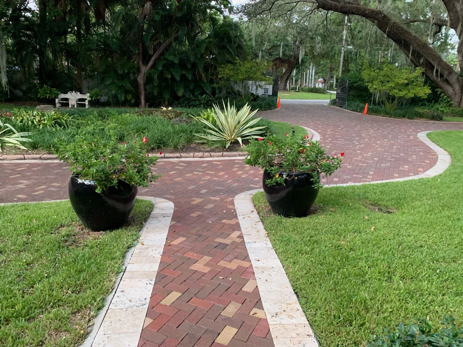 Curved brick garden path through a green park with potted plants and trees
