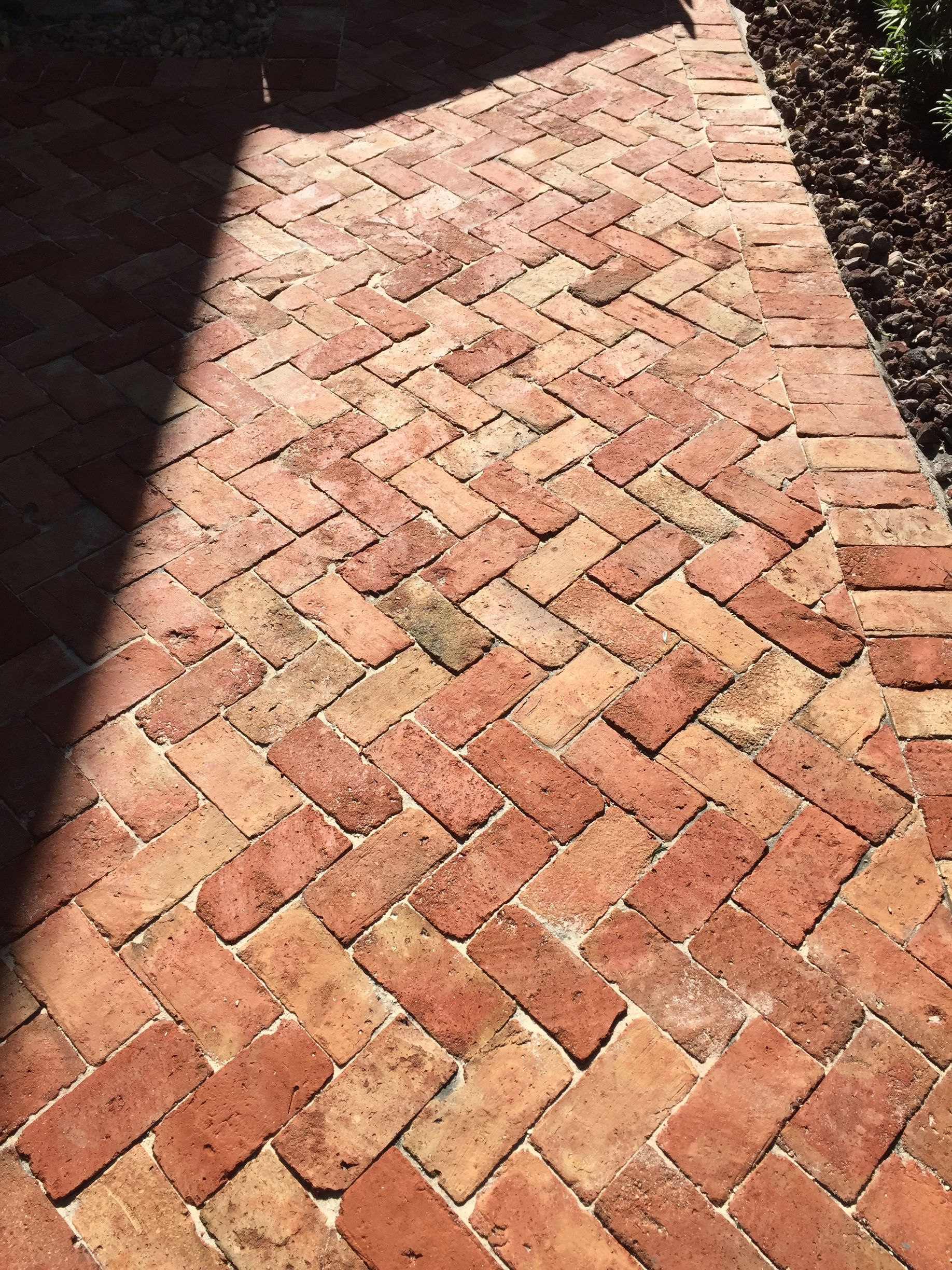 Sunlit red brick walkway in a herringbone pattern with a shadow across the left side