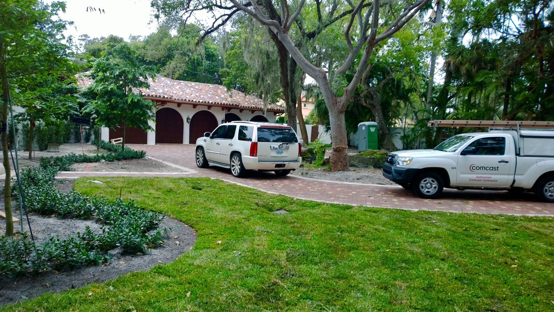 Two white SUVs parked on a driveway beside a pink house with trees and a green lawn