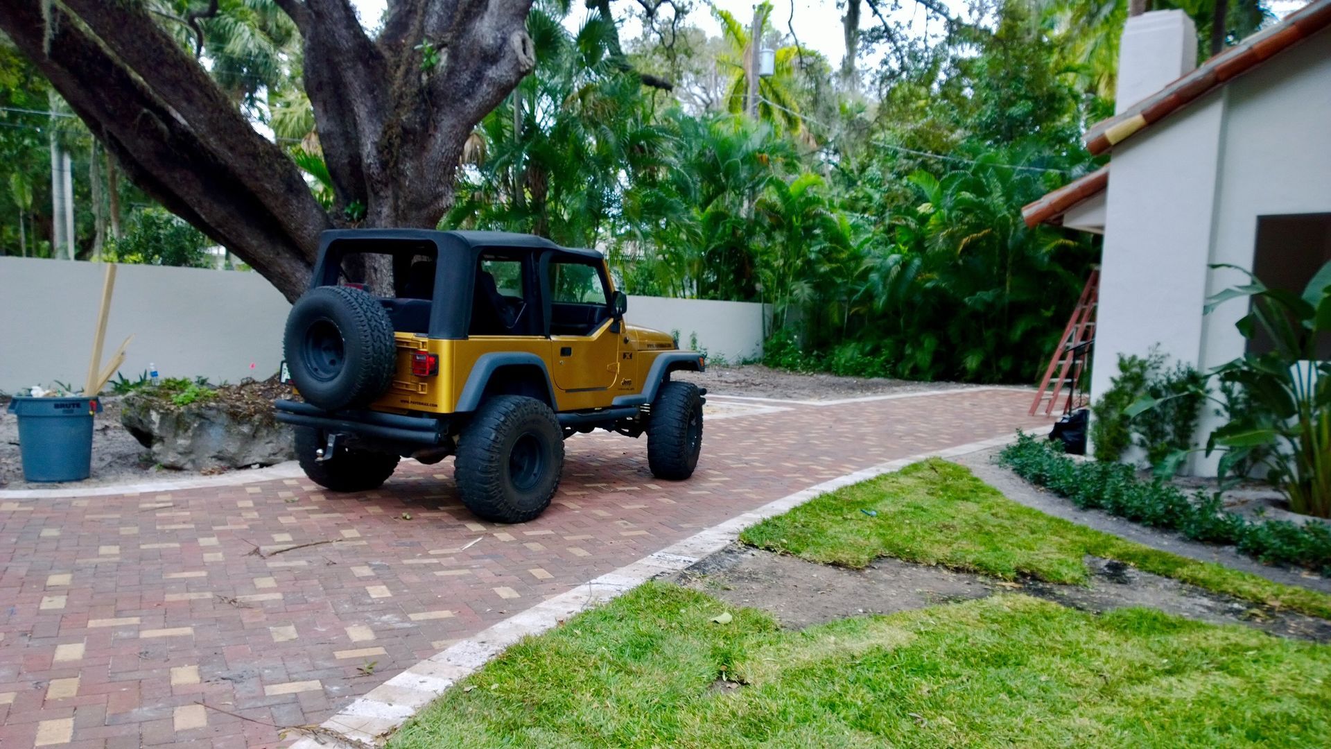 Yellow and black off-road Jeep parked on a brick driveway beside a house and greenery