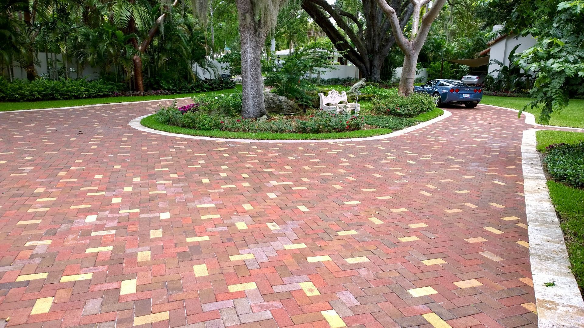 Curved brick driveway bordered by grass and trees, with a parked black car in the background.