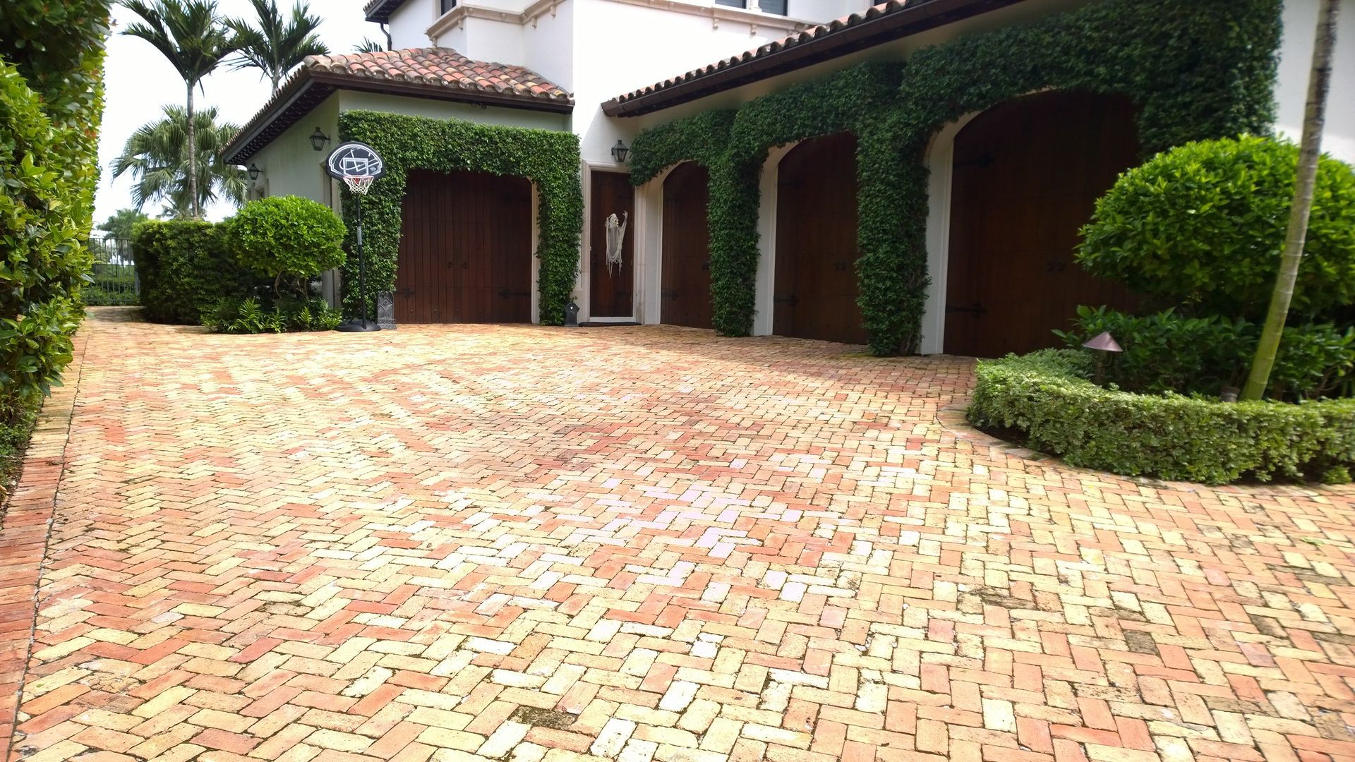 Brick driveway leading to a Mediterranean-style house with ivy-covered walls and arched garage doors