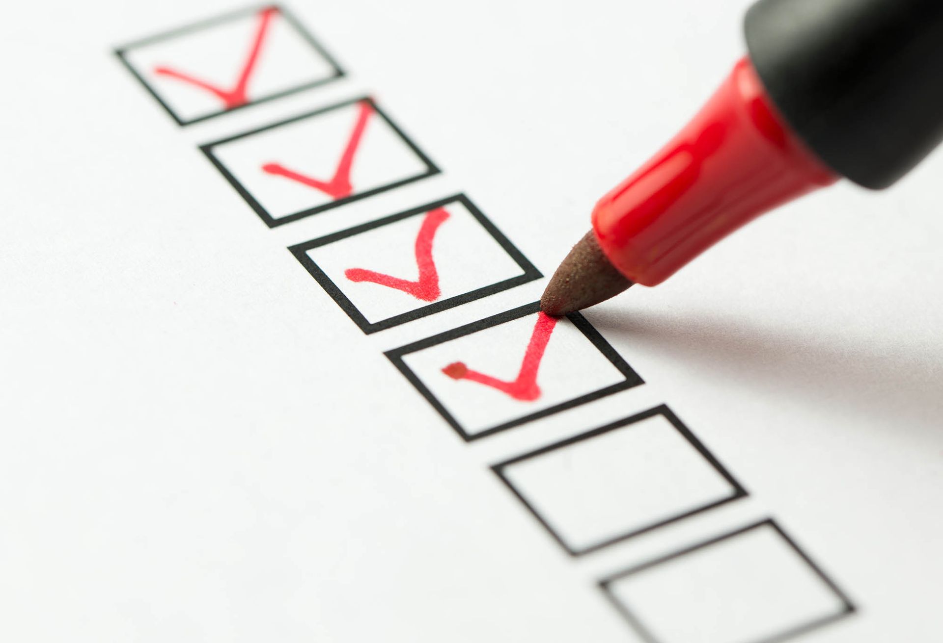 Red pen marking checkboxes on a checklist, with several red checkmarks and one blank box. Red pen marking checkboxes on a checklist, with several red checkmarks and one blank box.