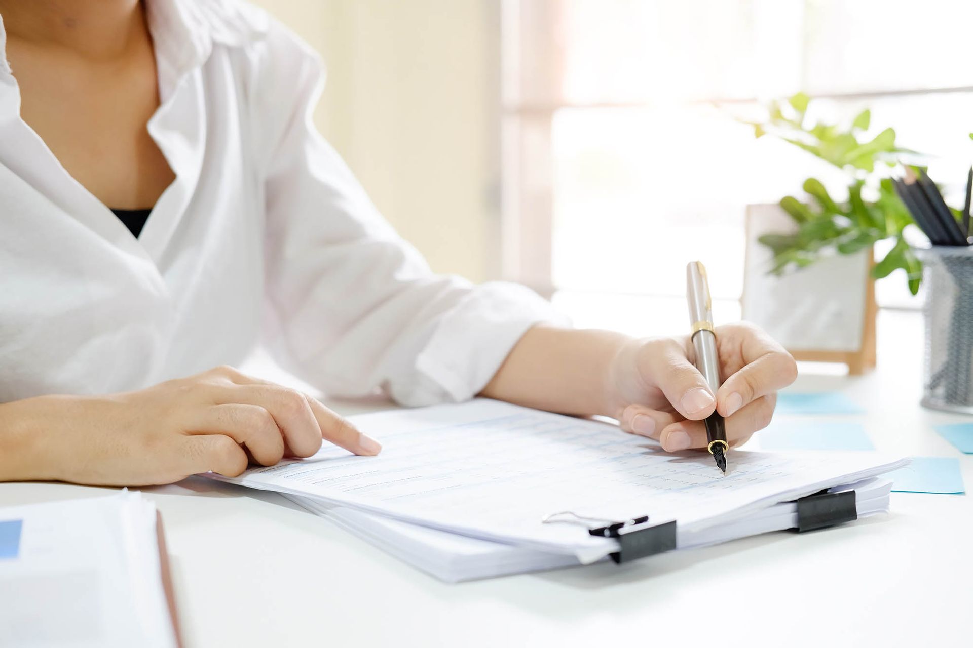 Person writing on a clipboard at a bright desk with a white shirt Person writing on a clipboard at a bright desk with a white shirt