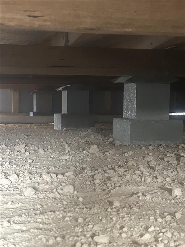 Under a low wooden structure, gravel ground with concrete supports and dark shadowed space beneath.